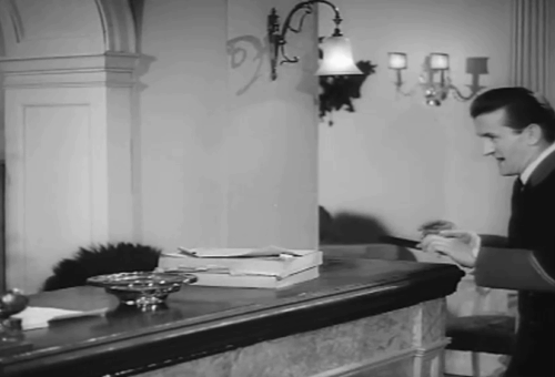 Force's Sweetheart - concierge Graham Stark placing black cat on hotel front desk animated gif