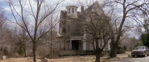 The House by the Cemetery - black cat lying by gravestone near house animated gif