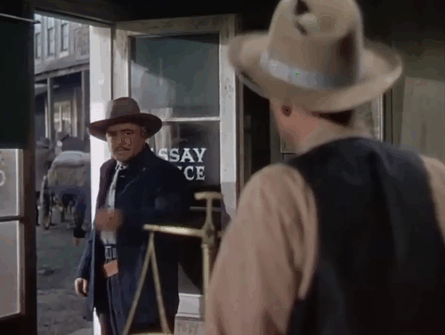 Relentless - camera pans by grey and white tabby cat in assayer office window animated gif