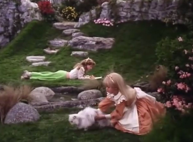 Alice in Wonderland - Alice Natalie Gregory reaching to pick up Persian white cat Dinah on grass
