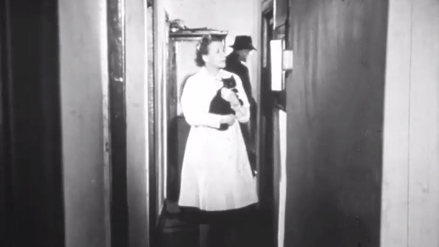 All Living Things - woman in lab coat carrying tuxedo cat in hallway