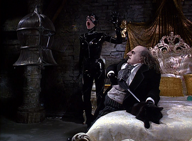 Batman Returns - Catwoman Michelle Pfeiffer opens mouth to release bird with Penguin Danny DeVito threatening black cat on bed