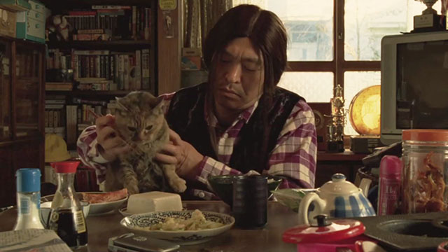 Big Man Japan - Masura Big Man Hitoshi Matsumoto at dinner table with torbie cat