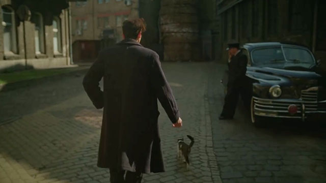The Brutalist - László walking down street past limousine with tabby and white cat