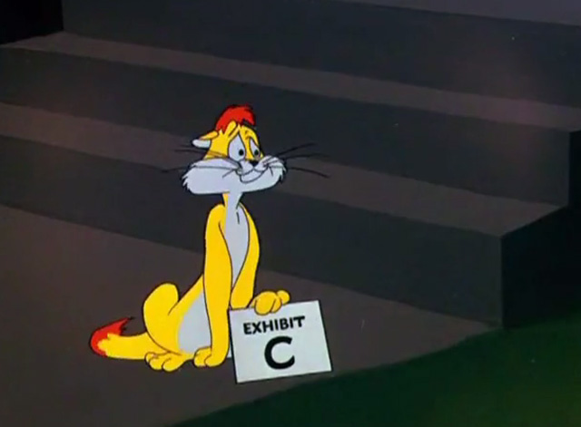 Cheese Chasers - cat Claude sitting and holding an Exhibit C sign