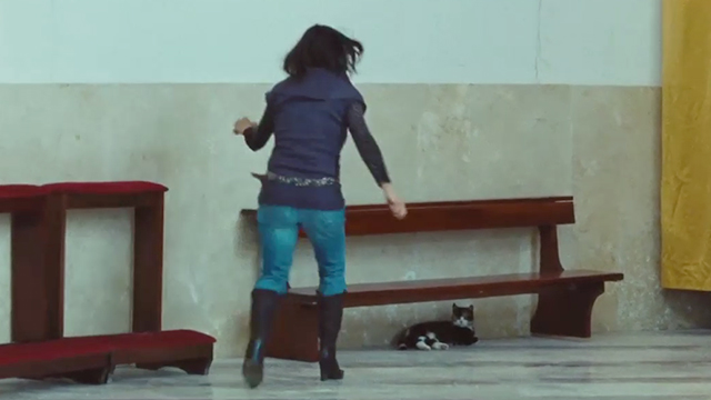 Corpo Celeste - girl running toward tortoiseshell and white cat under bench