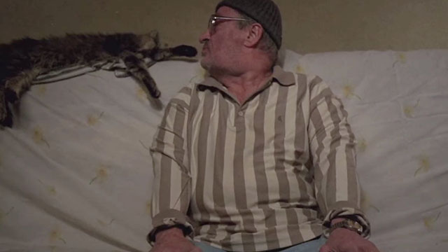 The Death of Mr. Lazarescu - Ion Fiscuteanu sitting on couch with brown tabby cat Mirandolina sleeping on back