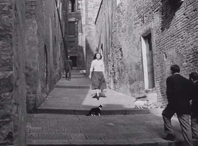 Deported - Gina Marina Berti walking down street toward black and white tuxedo cat