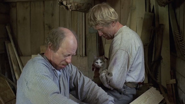 The Emigrants - Karl Max von Sydow holding white and tabby cat in barn with Nils Sven-Olof Bern