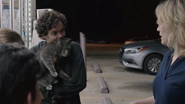 Family - Evil Eddie Christian Noël holding one eyed gray tabby cat Fartosaurus with Kate Taylor Schilling outside gas station mart