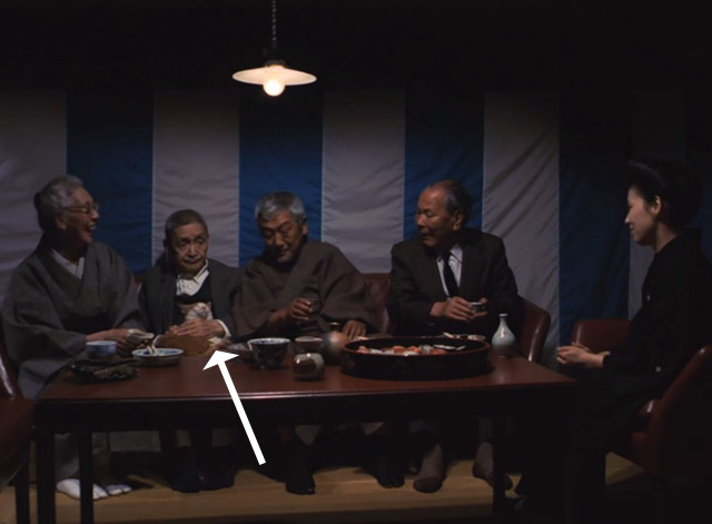 The Funeral - orange and white cat Kichi on lap of elderly man sitting at table with other people