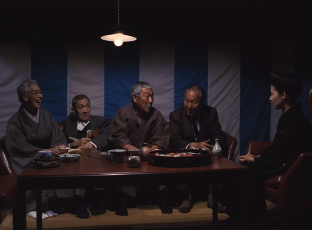 The Funeral - orange and white cat Kichi on lap of elderly man sitting at table with other people