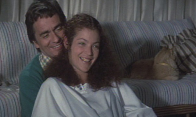 Micki and Maude - orange long-haired cat lying on couch behind Rob Dudley Moore and Maude Amy Irving