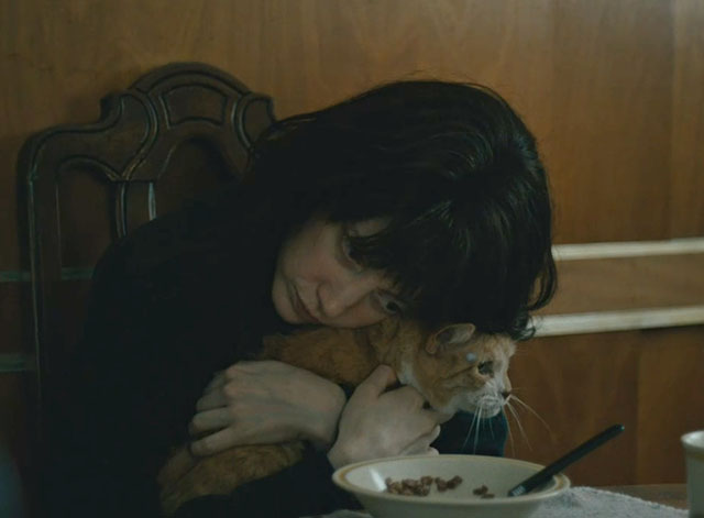 Nancy - Andrea Riseborough holding ginger and white tabby cat Paul at table