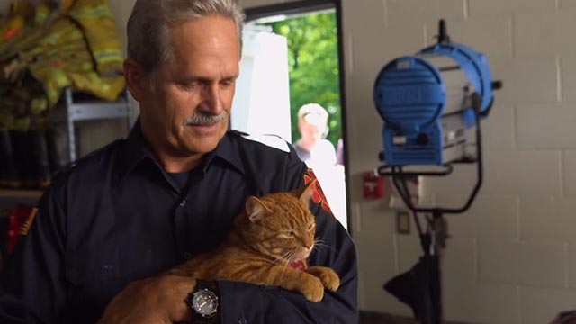 The Nine Lives of Christmas - orange tabby cat Ambrose Trace held by Chief Sam Gregory Harrison