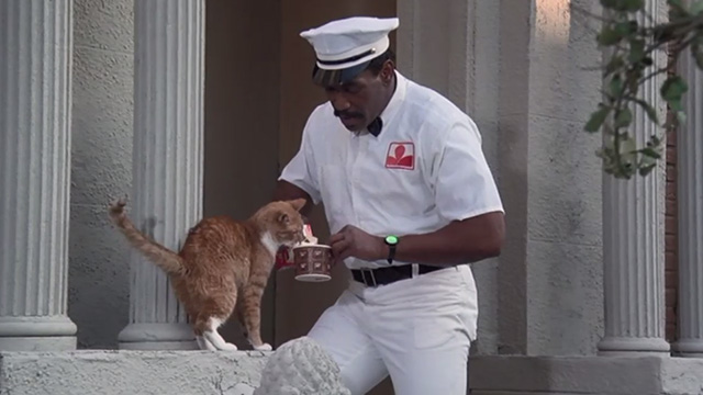 Police Academy 6: City Under Siege - Hightower Bubba Smith dressed as milkman pouring milk for orange tabby cat on steps