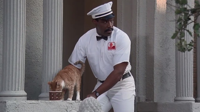 Police Academy 6: City Under Siege - Hightower Bubba Smith dressed as milkman with orange tabby cat drinking milk on steps