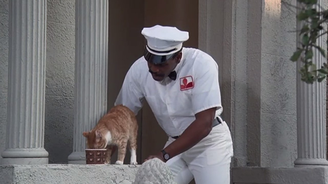 Police Academy 6: City Under Siege - Hightower Bubba Smith dressed as milkman with orange tabby cat drinking milk on steps