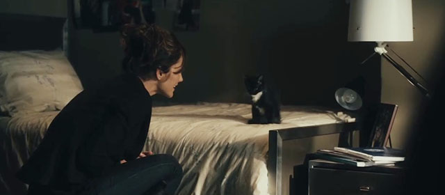 The Roommate - Sara Minka Kelly looking at tuxedo kitten Cuddles on bed