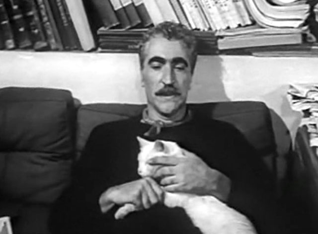 Les sept péchés capitaux - The Seven Deadly Sins - Olivier Orféo Tamburi sitting on couch with white cat Saha on lap