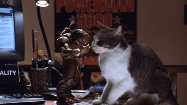 Small Soldiers - gray and white tabby cat beside Archer toy Gorgonite on desk