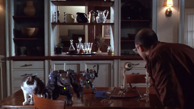 Small Soldiers - Irwin David Cross looking at Gorgonites and gray and white tabby cat on table
