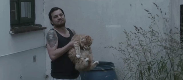 Tore tanzt - Nothing Bad Can Happen - Benno Sascha Alexander Gersak holding longhair ginger tabby cat beside rain barrel