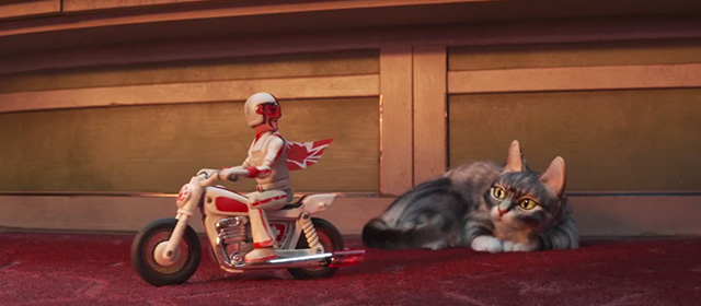 Toy Story 4 - tabby cat Dragon looking up at Duke Kaboom riding away on motorcycle