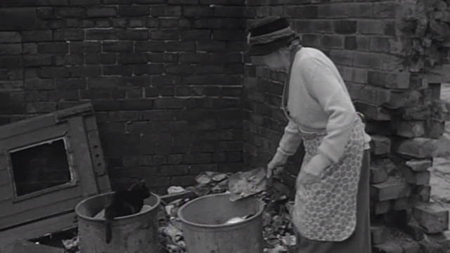 The Whisperers - black cat eating from garbage can beside Mrs. Ross Edith Evans