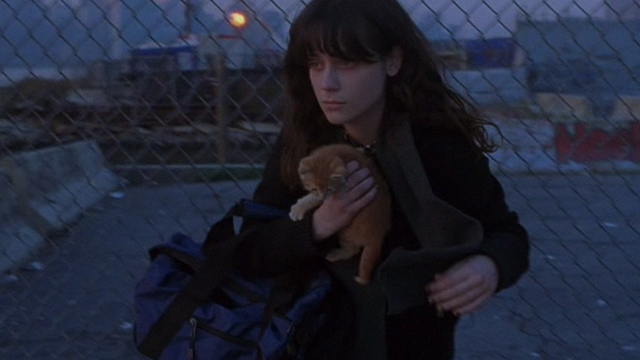 Winter Passing - Reese Zooey Deschanel moving through hole in chain link fence with orange tabby kitten Spike on bed