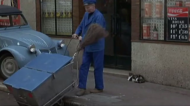 Without Apparent Motive - tabby and white cat sitting on sidewalk as street cleaner moves push cart