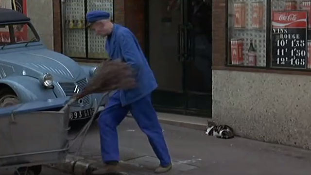 Without Apparent Motive - tabby and white cat sitting on sidewalk as street cleaner moves push cart