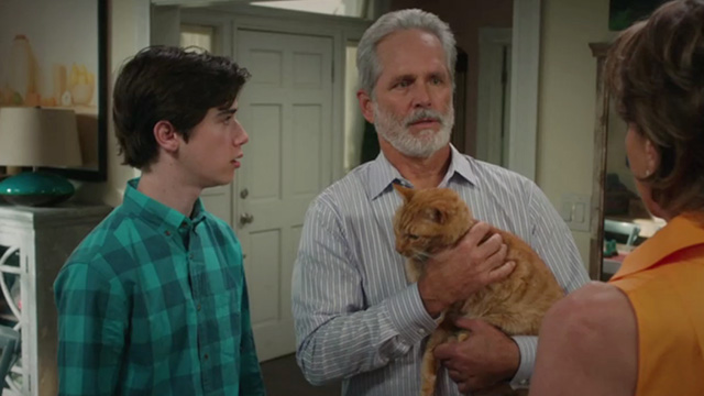 American Housewife - Grandma's Way - Kathryn Wendie Malick turning down Dan Gregory Harrison holding ginger tabby cat Mittens with Oliver Daniel DiMaggio