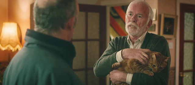 Derry Girls - The Night Before - Joe Ian Mcelhinney holding ginger tabby cat Seamus with Gerry Tommy Tiernan