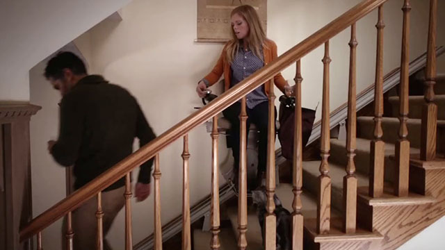 Don't Trust the B---- in Apartment 23 - It's a Miracle - June Dreama Walker riding stairlift chair up stairs as Michael Landes comes down stairs with tabby cat Freckles watching