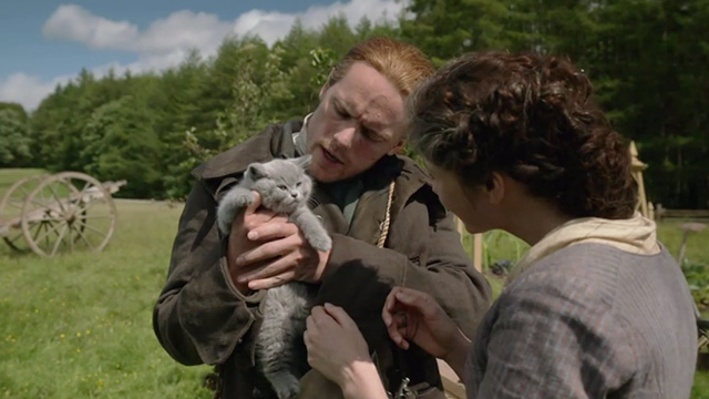 Outlander - Perpetual Adoration - Jamie Sam Heughan holding English shorthair kitten Adso Bear with Claire Caitriona Balfe