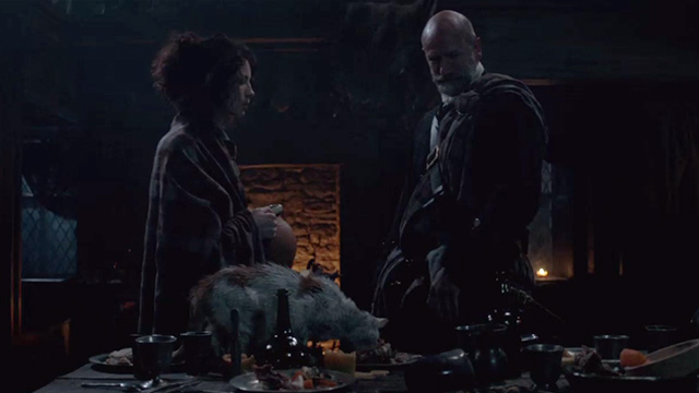 Outlander - The Wedding - dirty orange and white cat eating off leftover wedding scraps on table in front of Claire Caitriona Balfe and Dougal Graham McTavish