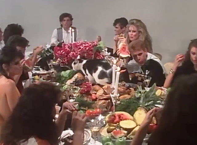 The One Thing - INXS - band members with women and a gray and white marbled cat feasting at table